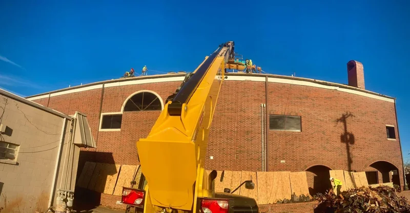 Crane lifting roofing materials to a crew on a large brick building
