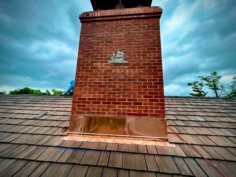 Brick chimney with newly installed copper flashing on a synthetic shake roof