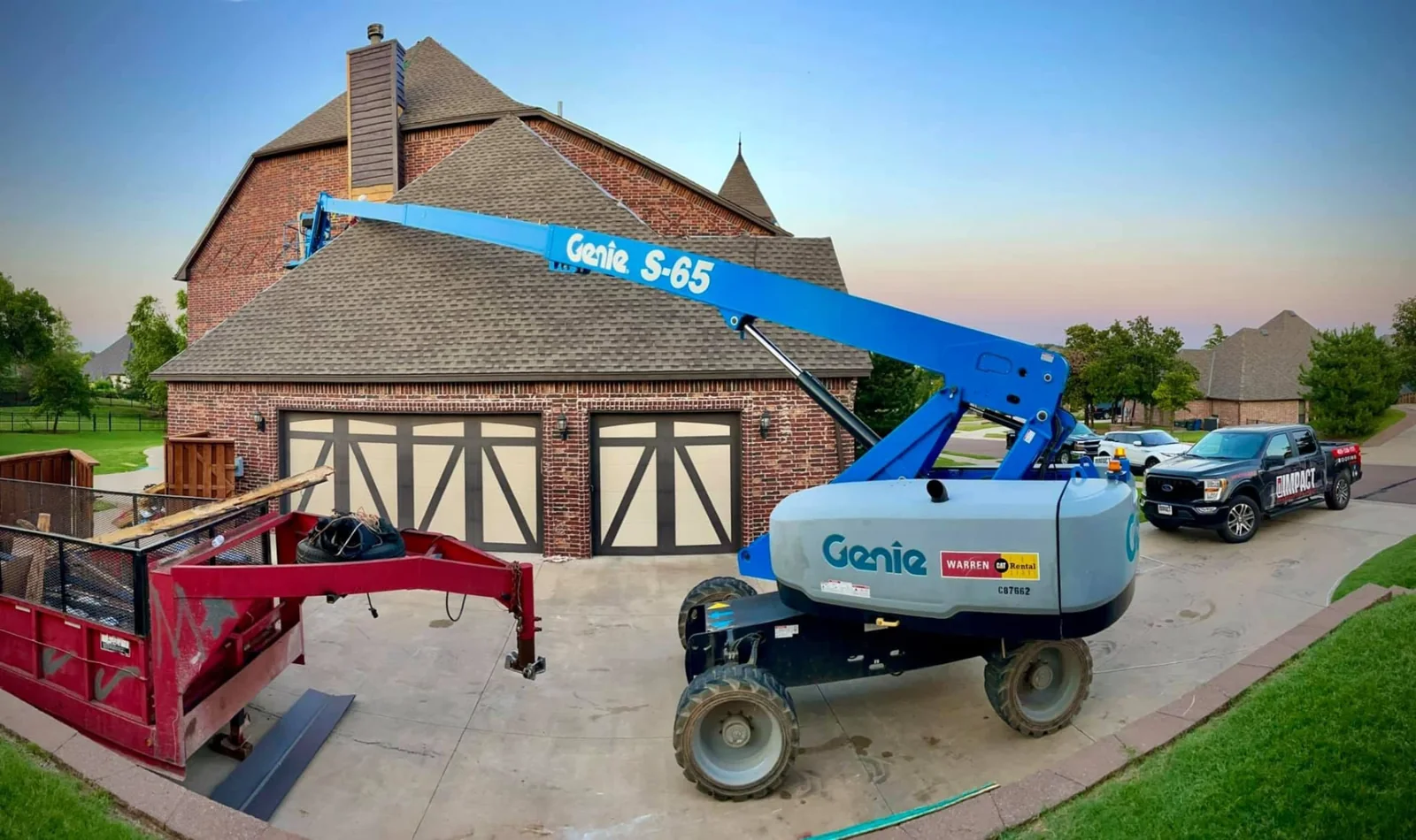 Boom lift and roofing equipment beside a large brick home during installation