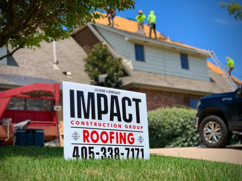 Roofing crew replacing the roof of a brick home behind an Impact yard sign