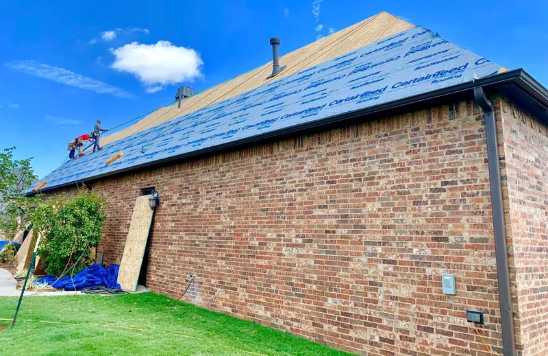 Roofers installing synthetic underlayment on a brick home